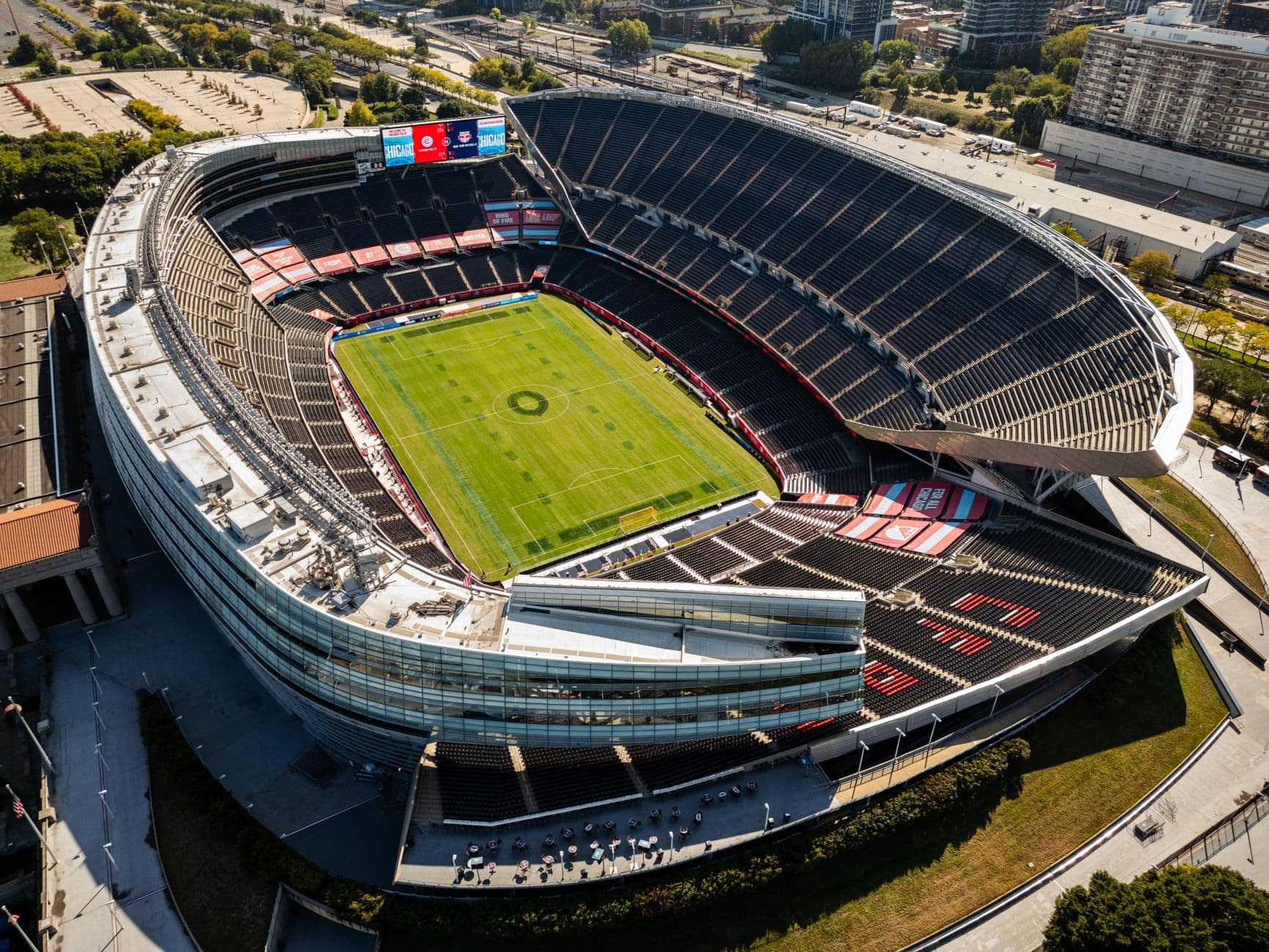 Aerial shot of a modern, empty soccer stadium surrounded by city buildings on a clear day.