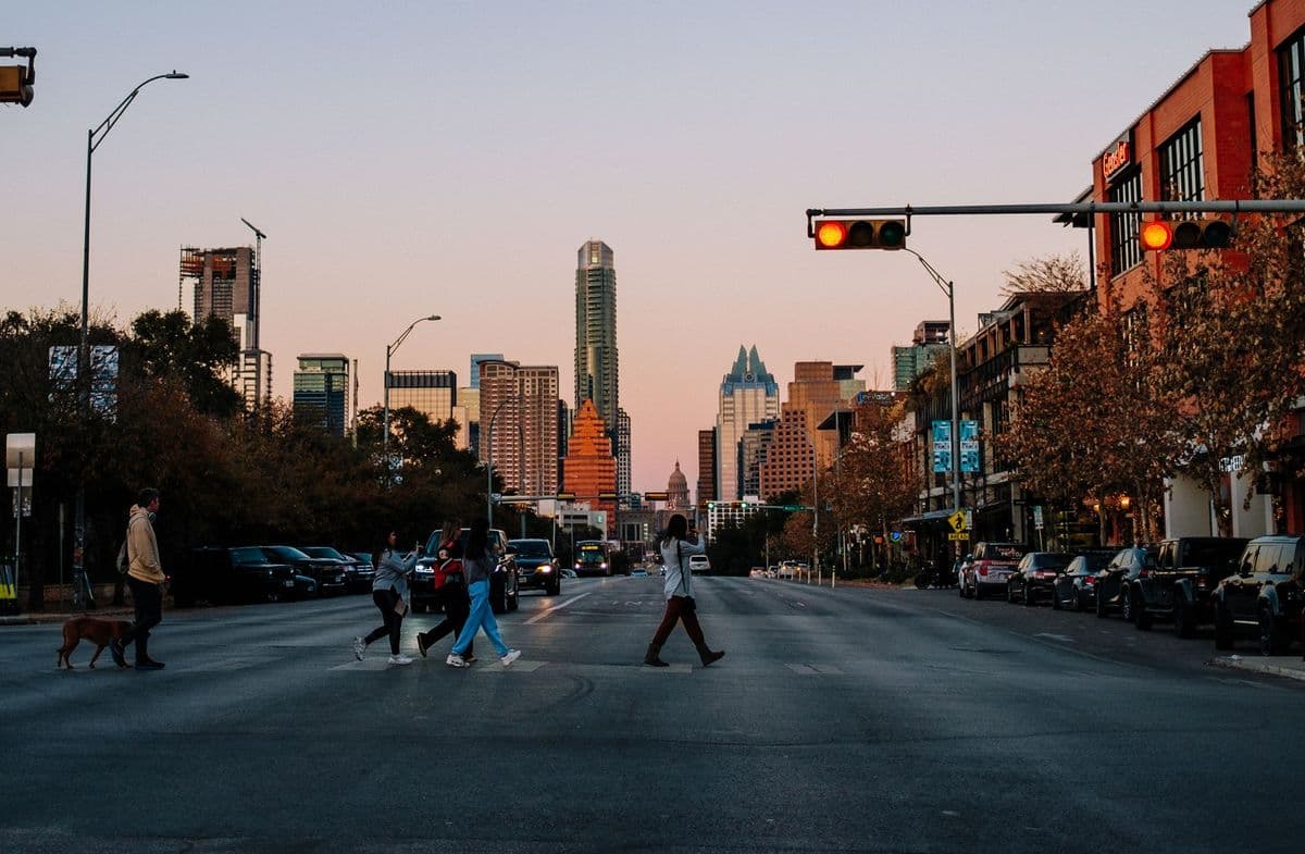 People crossing a city street in Austin, Texas at sunset with the skyline in the background.